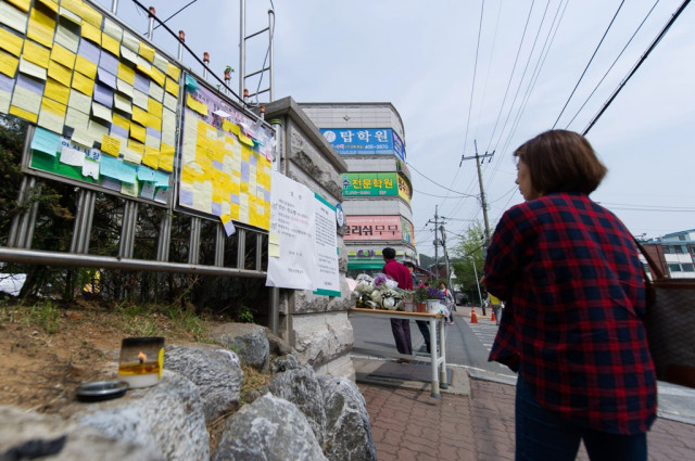 a woman looks at messages and flowers left at a makeshift memorial at the main gate of danwon high school in ansan photo afp a woman looks at messages and flowers left at a makeshift memorial at the main gate of danwon high school in ansan photo afp