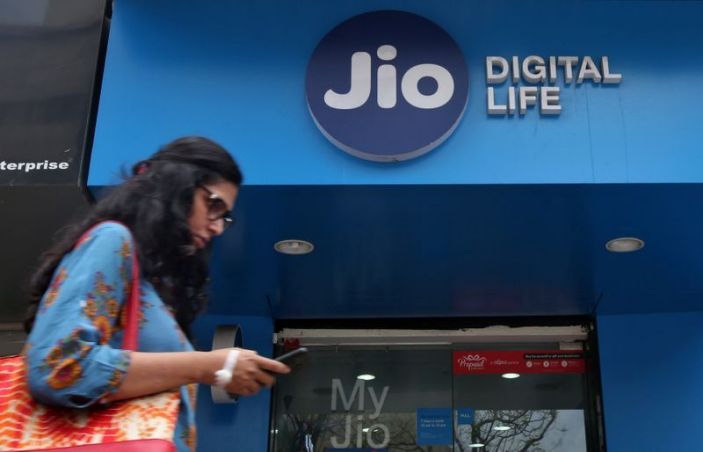 a woman checks her mobile phone as she walks past a mobile store of reliance industries jio telecoms unit in mumbai reuters
