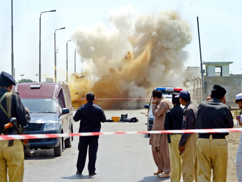 police officials watch as smoke and dust billows after bomb experts detonated an explosive device near an oil terminal in karachi photo afp