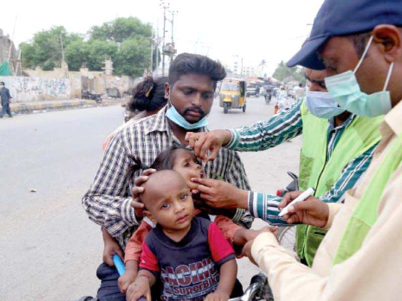 a vaccinator administers oral polio vaccine to a child going on a motorbike with his parents on a street in karachi on monday photo ppi