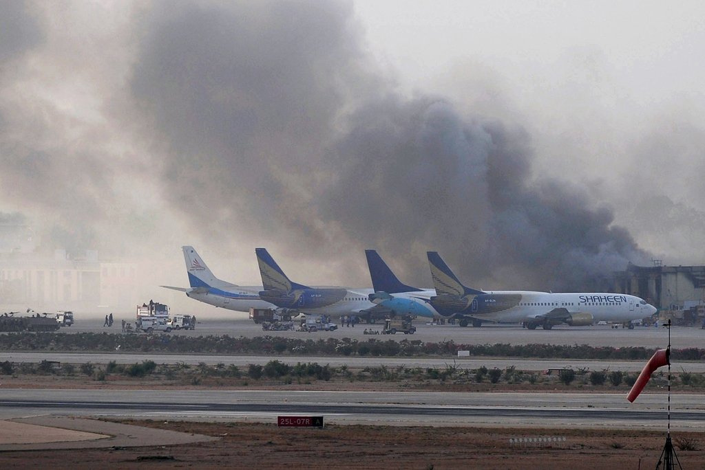 people look on as smoke rises after militants launched an early morning assault at jinnah international airport in karachi on june 9 2014 photo afp