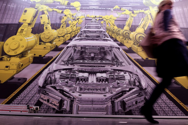 a woman passes a poster showing a production line with robots at the hanover trade fair in hanover germany march 31 2019 photo reuters a woman passes a poster showing a production line with robots at the hanover trade fair in hanover germany march 31 2019 photo reuters