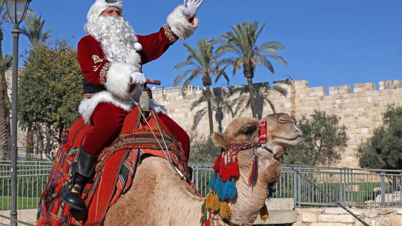 Issa Kassissieh, dressed as Santa Claus, poses for a picture as he rides a camel at Jaffa Gate in Jerusalem's Old City © AHMAD GHARABLI / AFP