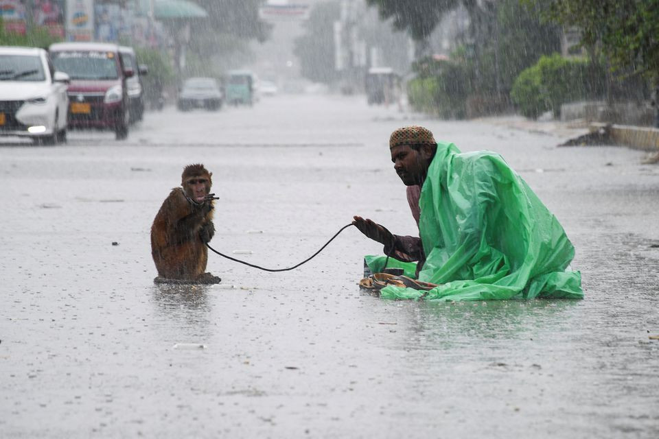 A man sits with his pet monkey, as they seek charity from passersby, along a road amidst rainfall during the monsoon season in Hyderabad, Pakistan August 24, 2022. REUTERS