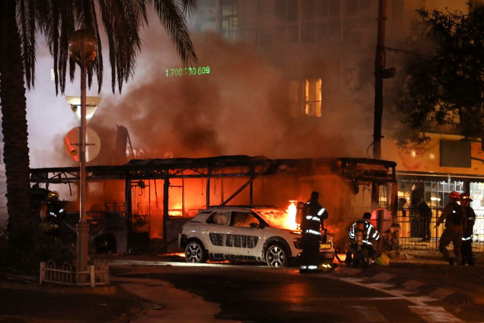 Israeli firefighters, security and rescue forces stand next to a burning bus and car that were hit by a rocket fired from Gaza towards Holon, Israel May 11, 2021. PHOTO: REUTERS