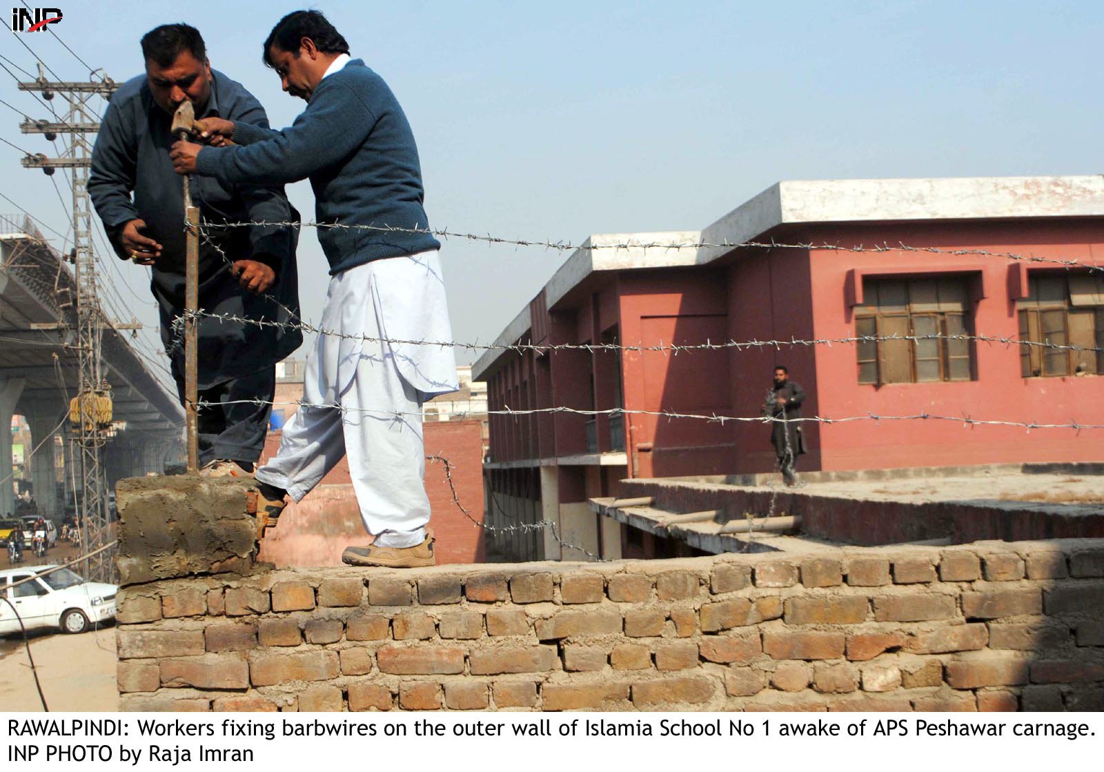 two men put up barbed fencing on the boundary wall of a school photo inp