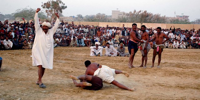 a happy referee the referee waves his arms in the air as two mulh wrestlers grapple photo courtesy abid arshad
