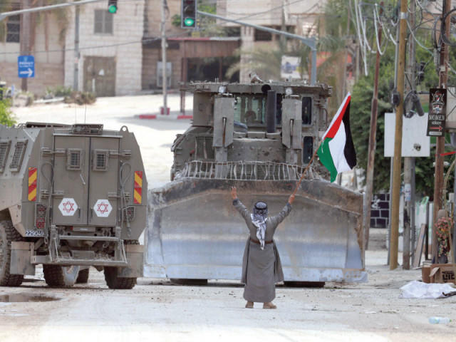 a palestinian man lifts a national flag and flashes the victory sign as israeli armoured vehicles drive on a street during a raid in tulkarem in the occupied west bank photo afp a palestinian man lifts a national flag and flashes the victory sign as israeli armoured vehicles drive on a street during a raid in tulkarem in the occupied west bank photo afp