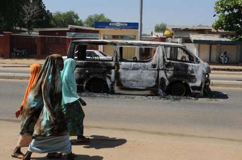 young girls walk past a vehicle burnt on a street of damaturu yobe state northeastern nigeria on november 7 2011 photo afp