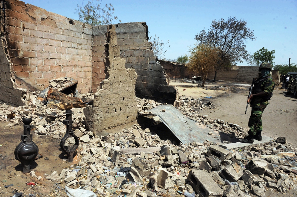 in this file photo a soldier stands beside a house burnt during clashes between insurgents and soldiers on april 25 2013 in the remote northeast town of baga borno state in nigeria