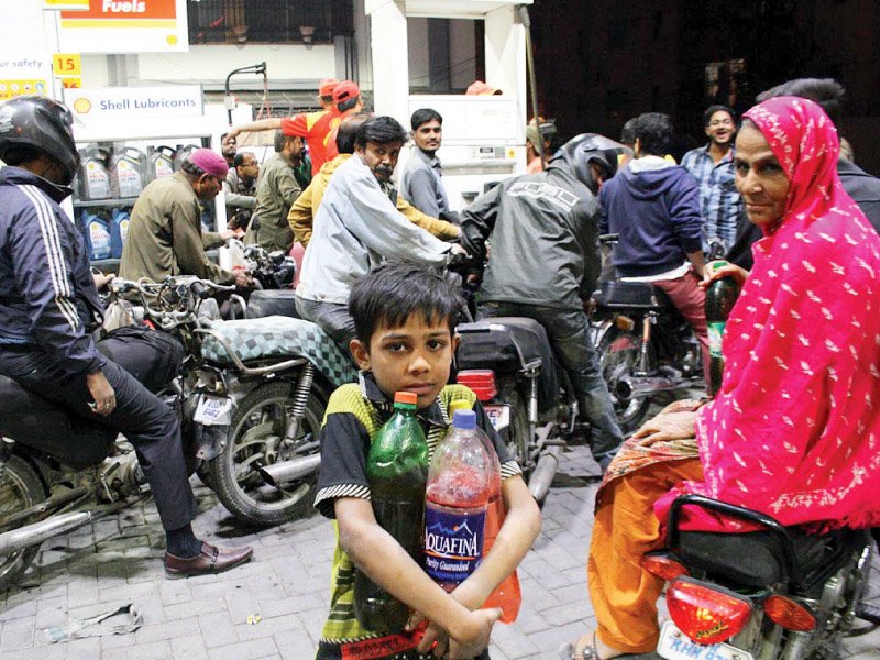 a boy clutches onto bottles filled with petrol as motorists queue up at a fuel station in karachi photo online