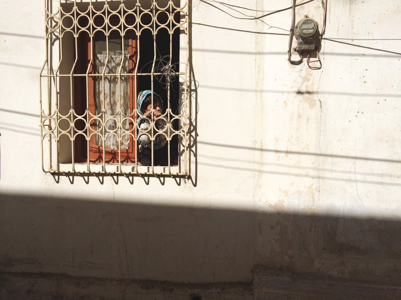 a child looks out from the ground level window of his house in the street where policeman shahmir was killed on monday photo tooba masood express