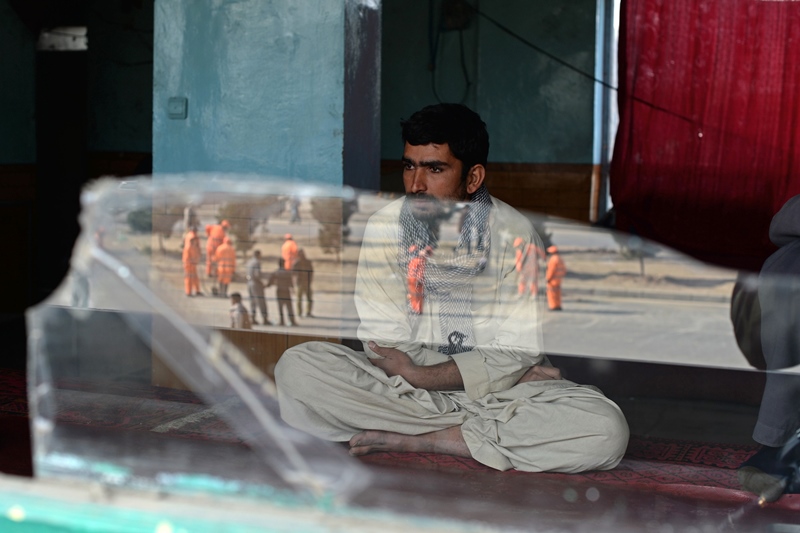 in this photograph taken on october 14 2014 an afghan resident looks on as the scene of a blast site is reflected on a broken window following an explosion from a magnetic bomb attached to a civilian car in kabul the number of civilians killed and wounded in afghanistan jumped 22 percent in 2014 the un said february 18 2015 as nato troops withdrew from combat leaving government forces to battle a raging taliban insurgency photo afp