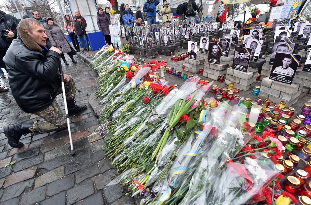 a man kneels in front of the quot heavenly hundred quot monument set for killed maidan activists in kiev on february 20 2015 during memorial ceremony marking the first anniversary of the killings of demonstrators in the final act of a dramatic uprising around independance square in kiev known as maidan photo afp