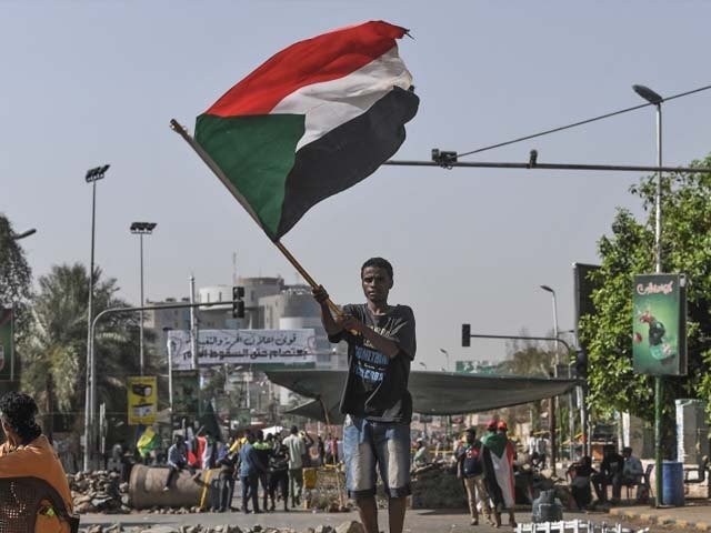 a sudanese protester waves a national flag near a makeshift barricade photo getty a sudanese protester waves a national flag near a makeshift barricade photo getty