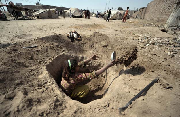 a pakistani child digs a hole to be used as a toilet for her family at a slum in multan on march 13 2012 photo afp
