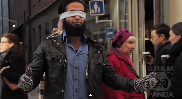 a blindfolded muslim man standing in the streets of stockholm with his arms stretched out asking for people to trust him