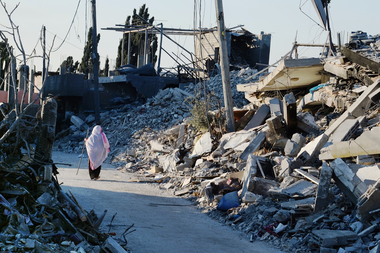 a palestinian woman uses a piece of reebar she found amid the rubble for support as she walks past destroyed homes in a street in beit hanun northern gaza strip on august 12 2014 photo afp