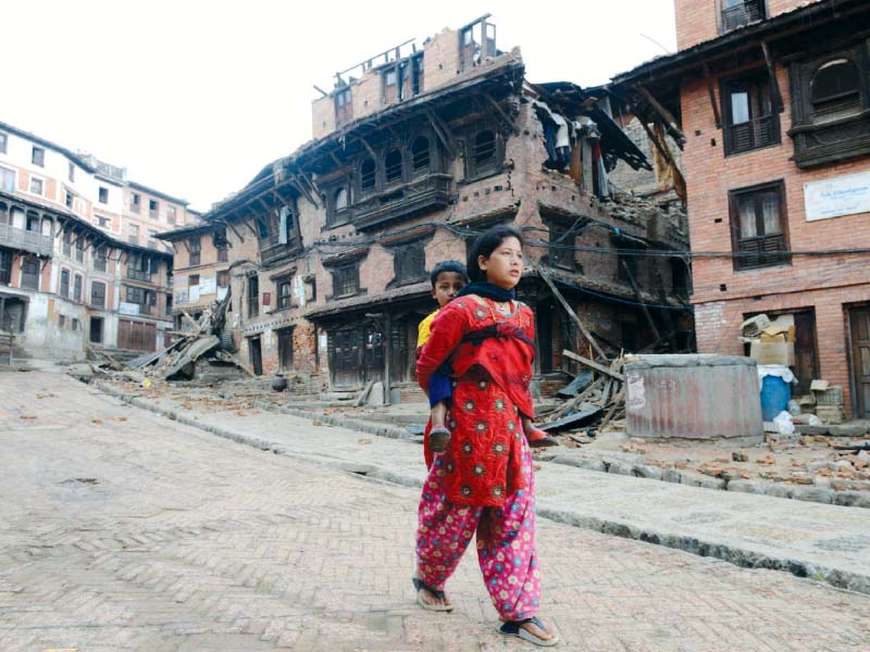 a woman carries a child next to collapsed houses on the outskirts of kathmandu photo afp