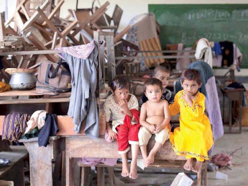 little children sit at a ramshackle school broken furniture and clothes are littered everywhere instead of children learning how to read and write photo file