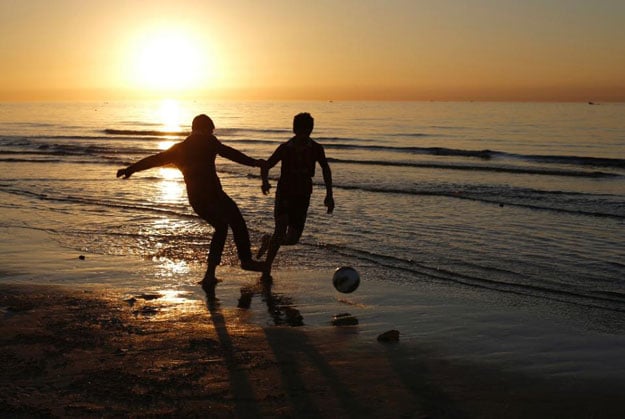 palestinians play football on a beach as the sun sets over gaza city on january 21 2015 photo afp