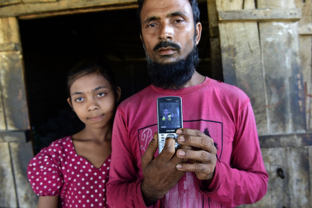 in this photo taken on may 15 2015 abdur rahman r father of 16 year old rohingya teenager muhammad shorif is watched by his daughter as he poses holding a mobile phone with an image of his son during an interview outside the nayapara rohingya camp in the southern bangladesh city of teknaf photo afp