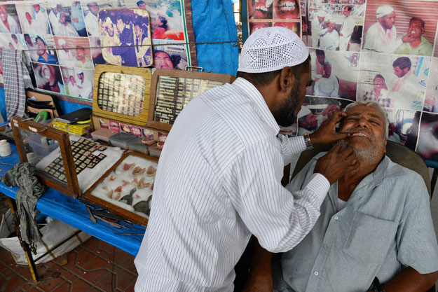 traditional indian dental worker allah baksh takes measurements for dentures from a customer at his roadside stall at k r market bus stand in bangalore ignoring noisy buses and curious onlookers street dentist allah baksh plunges his hands into a patient 039 s mouth to fit a sparkling set of dentures for 12 in the indian city of bangalore photo afp