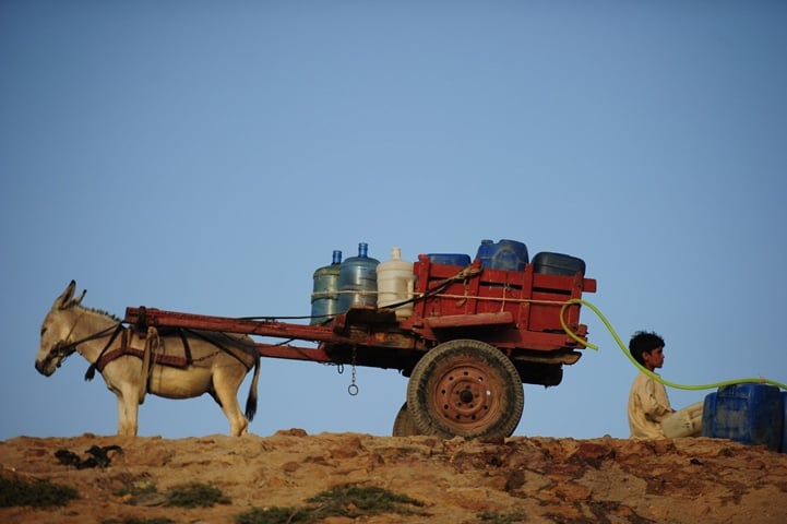 a pakistan youth sits next to his donkey cart loaded with containers near a water pipeline in karachi on may 5 2014 photo afp