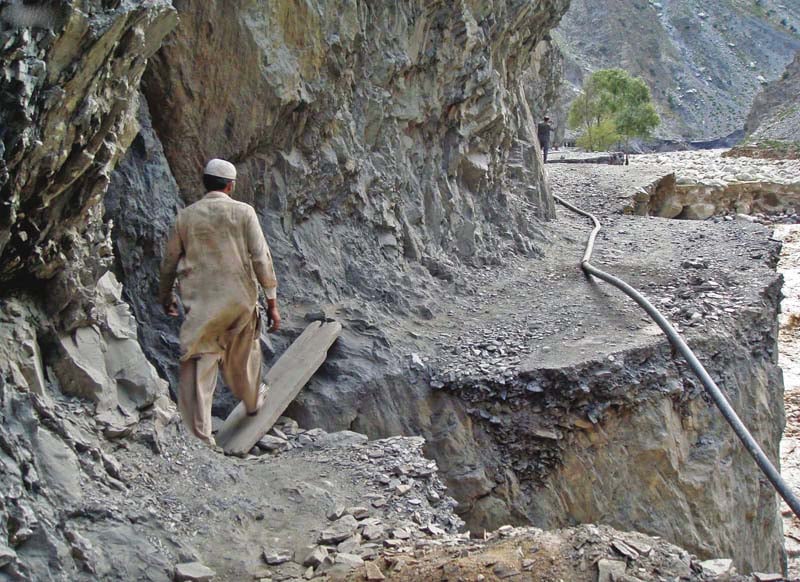 a man crosses a road damaged by floods in chitral photo inp