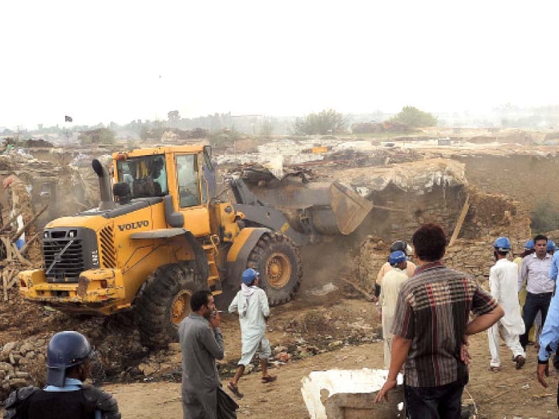 a bulldozer razes a slum to the ground a policewoman removes infants from a home a terrified child cries as a woman pleads to a policeman in the background a security official fires teargas shell at protesting dwellers photo online waseem nazeer express