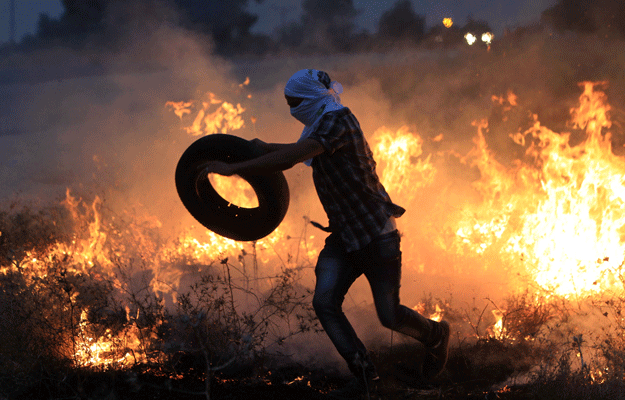 a palestinian protester throws a tire into a fire during clashes with israeli security forces following a protest in reaction to the death of the 18 month old child killed in an arson attack in the occupied west bank earlier in the week on august 2 2015 on a street leading to duma village photo afp