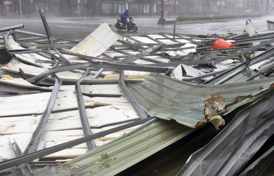 a motorcyclist rides past a damaged roof as typhoon soudelor hits taipei on august 8 2015 photo afp