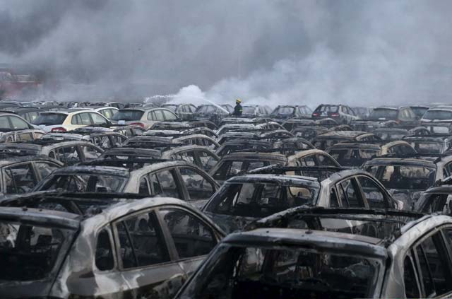 a firefighter works at the site near damaged vehicles as smoke arises from debris after the explosion at the binhai new district in tianjin photo reuters