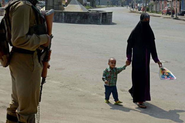 an indian paramilitary solider stands guard as kashmiri pedestrians walk along a street during a curfew in srinagar on aug 14 2015 photo afp