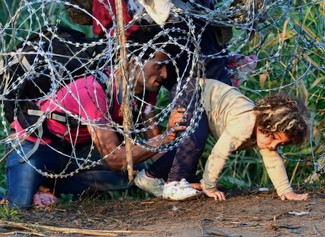 a young girl is helped by her father as they creep under a barbed fence near the village of roszke at the hungarian serbian border on august 27 2015 photo afp a young girl is helped by her father as they creep under a barbed fence near the village of roszke at the hungarian serbian border on august 27 2015 photo afp