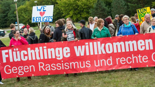 people hold up a banner which reads quot refugees welcome   against racism quot during a rally at the registry center for refugees in eisenhuettenstadt germany on september 9 2015 photo afp