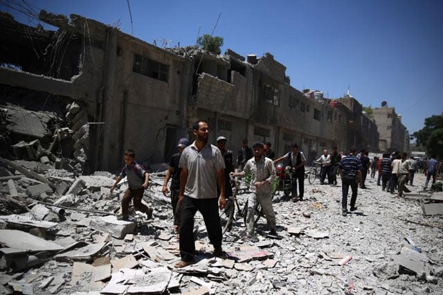 syrians walk amidst the rubble of buildings in the rebel held area of douma east of the syrian capital damascus following air strikes by regime forces on june 30 2015 photo afp