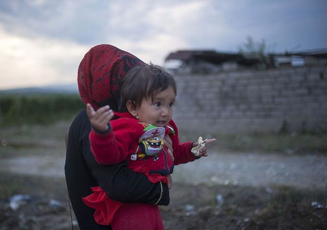 a woman carries a young girl as migrants and refugees cross the border between greece and macedonia near the town of gevgelija on september 11 2015 photo afp