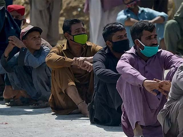 people sit in a line to receive free food donations in karachi photo afp