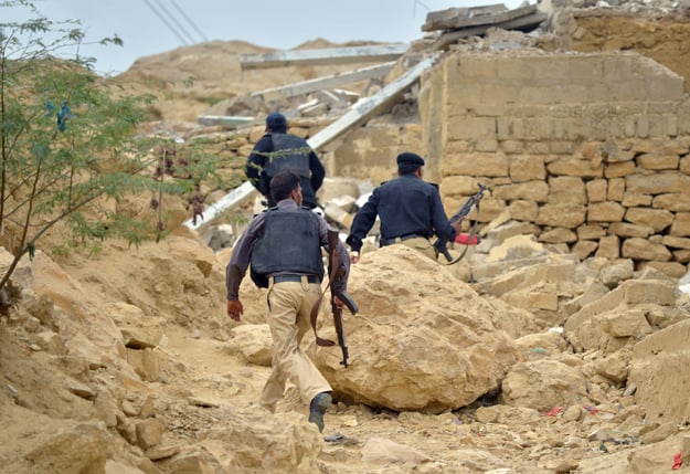 this photograph taken on august 21 2015 shows policemen taking a position at the destroyed hideouts of taliban militants in the manghopir area of karachi photo afp