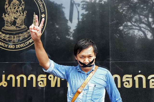 thai journalist pravit rojanaphruk flashes a v sign as he stands with his mouth taped outside a military base in bangkok where he had been summoned by the junta photo afp