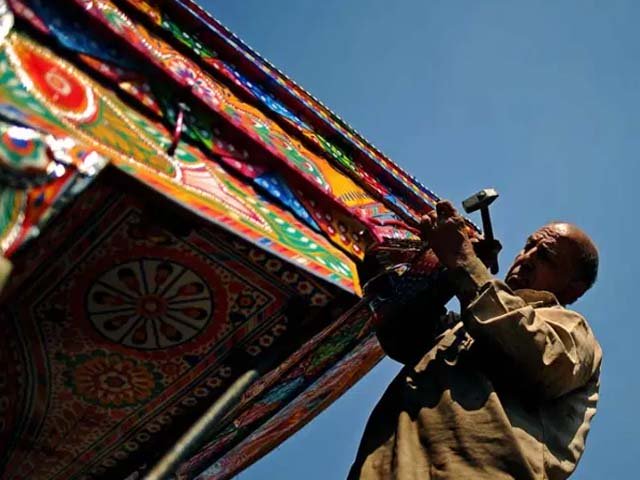 an electrician tacks electrical cables onto a decorated truck at a workshop in rawalpindi photo afp