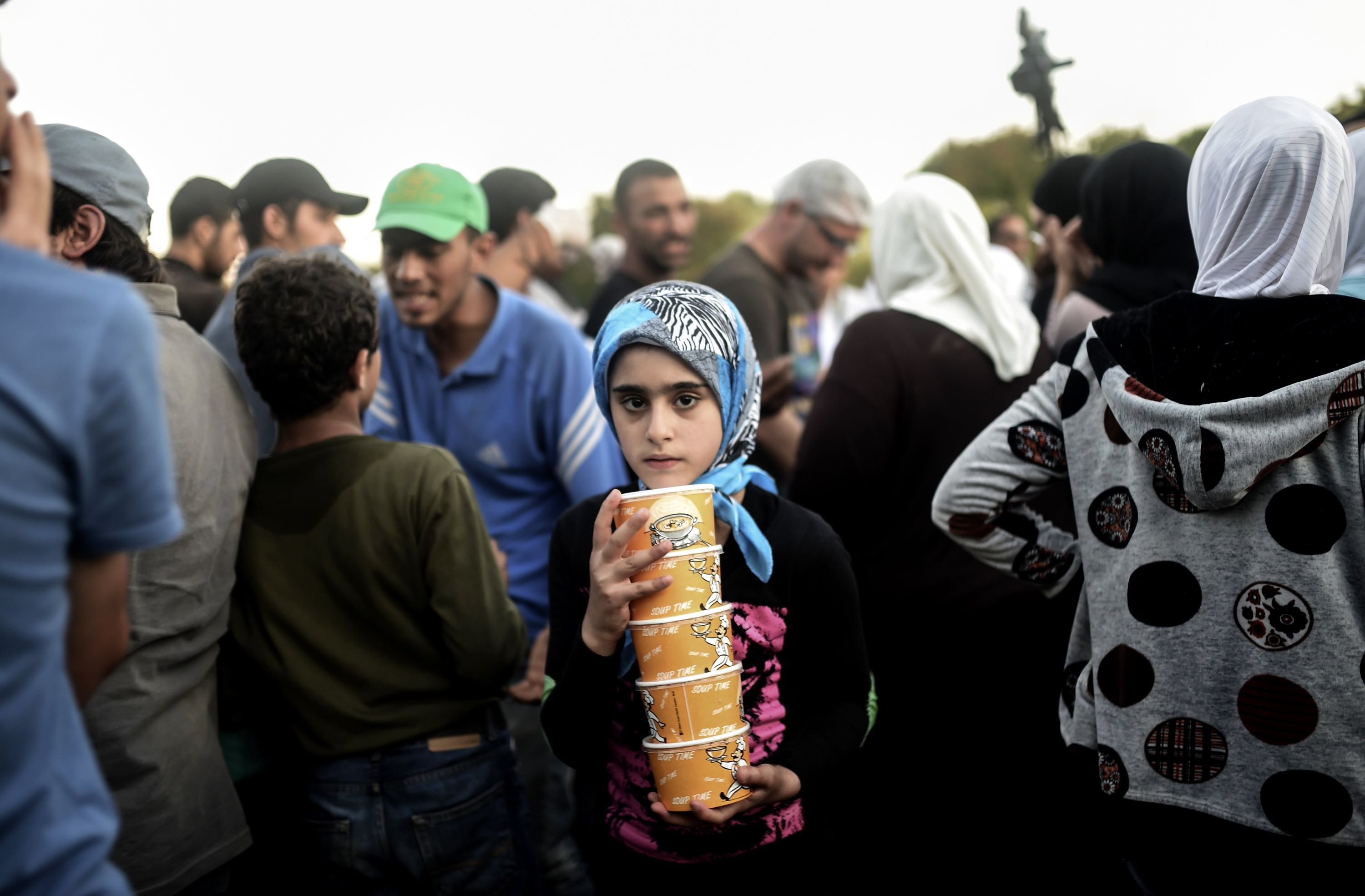 a girl carries cartons of soup as syrian refugees queue for food as they rest beside the highway on their way to the border between turkey and greece in edirne on september 17 2015 photo afp