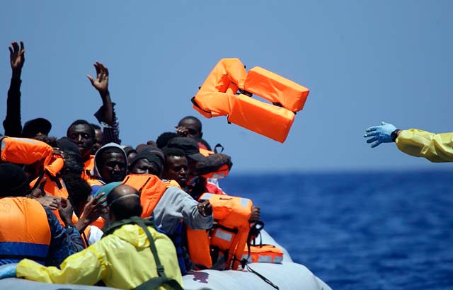 a belgian navy sailor tosses a life vest to migrants sitting in a rubber boat as they approach the belgian navy vessel godetia during a search and rescue mission in the mediterranean sea off the libyan coast on june 23 2015 photo afp