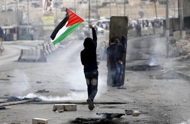 a palestinian protester holds a palestinian flag as others take cover during clashes with the israeli army at qalandia checkpoint near occupied west bank city of ramallah october 6 2015 photo reuters