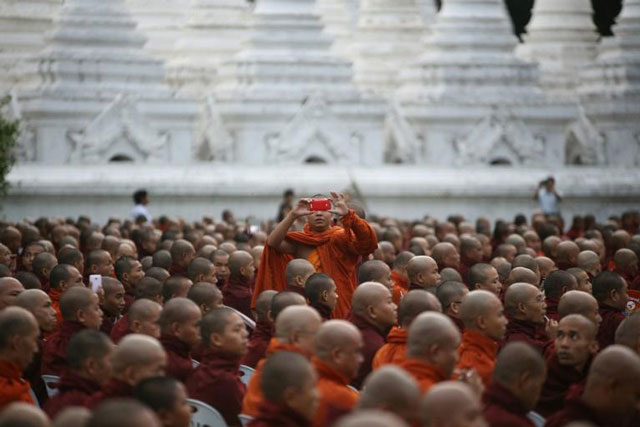 a buddhist monk takes a photo as he and other monks from myanmar and thailand are offered morning alms during the first ever myanmar thailand friendship service in mandalay photo afp