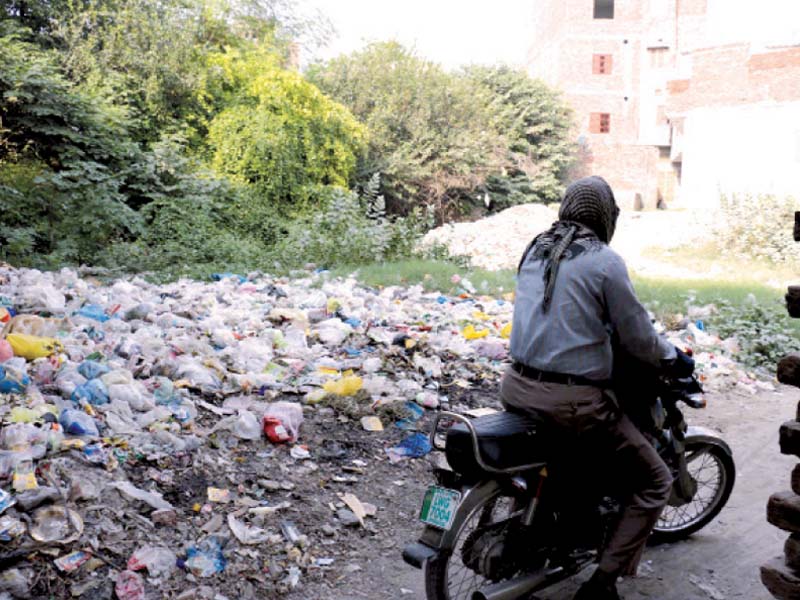 a motorcyclist rides past an open plot turned into solid waste dumping site near abbott road several voters have complained about lack of facilities in their areas to dump solid waste photo shafiq malik express