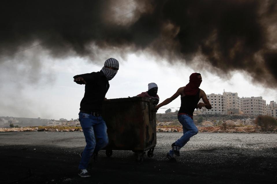 palestinian protesters pull a rubbish bin as they clash with israeli security forces in the west bank town of al bireh on the northern outskirts of ramallah on october 20 2015 photo afp