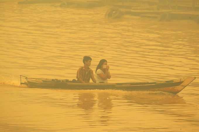 a couple crosses a river by boat as the city shrouded in thick yellow haze in palangkaraya on october 22 2015 photo afp