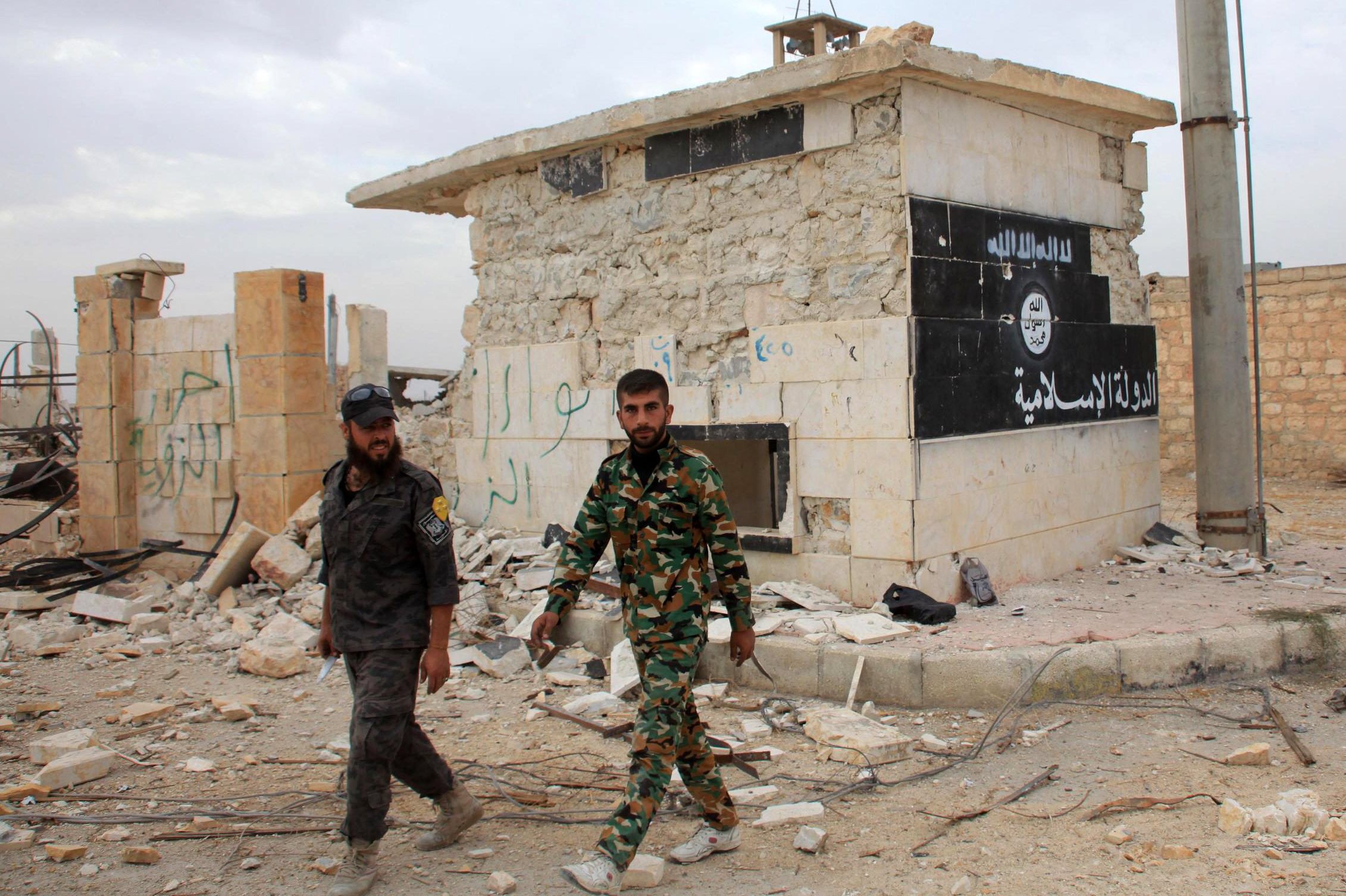 syrian government forces walk past a building bearing an image on the wall with islamic writing and reading in arabic the quot islamic state quot in the village of jabboul on the eastern outskirts of the northern syrian city of aleppo after taking control of the village from islamic state is group islamists on october 24 2015 photo afp